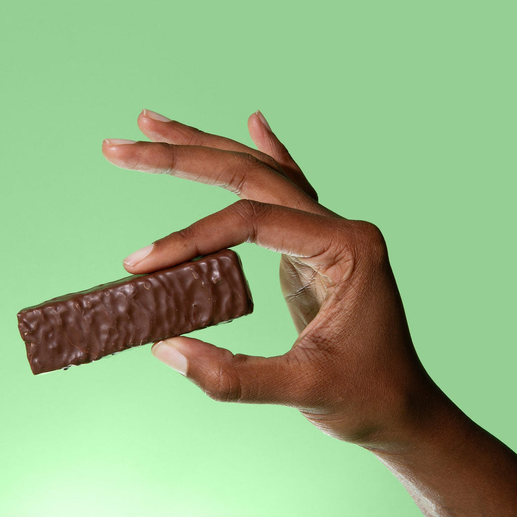 Hand holding a chocolate bar against a green background